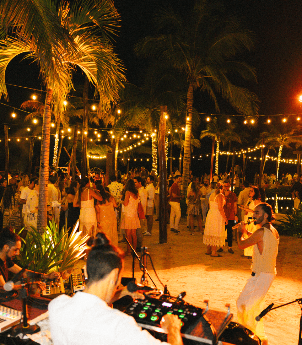 A DJ and dancers on the beach under palm trees at night