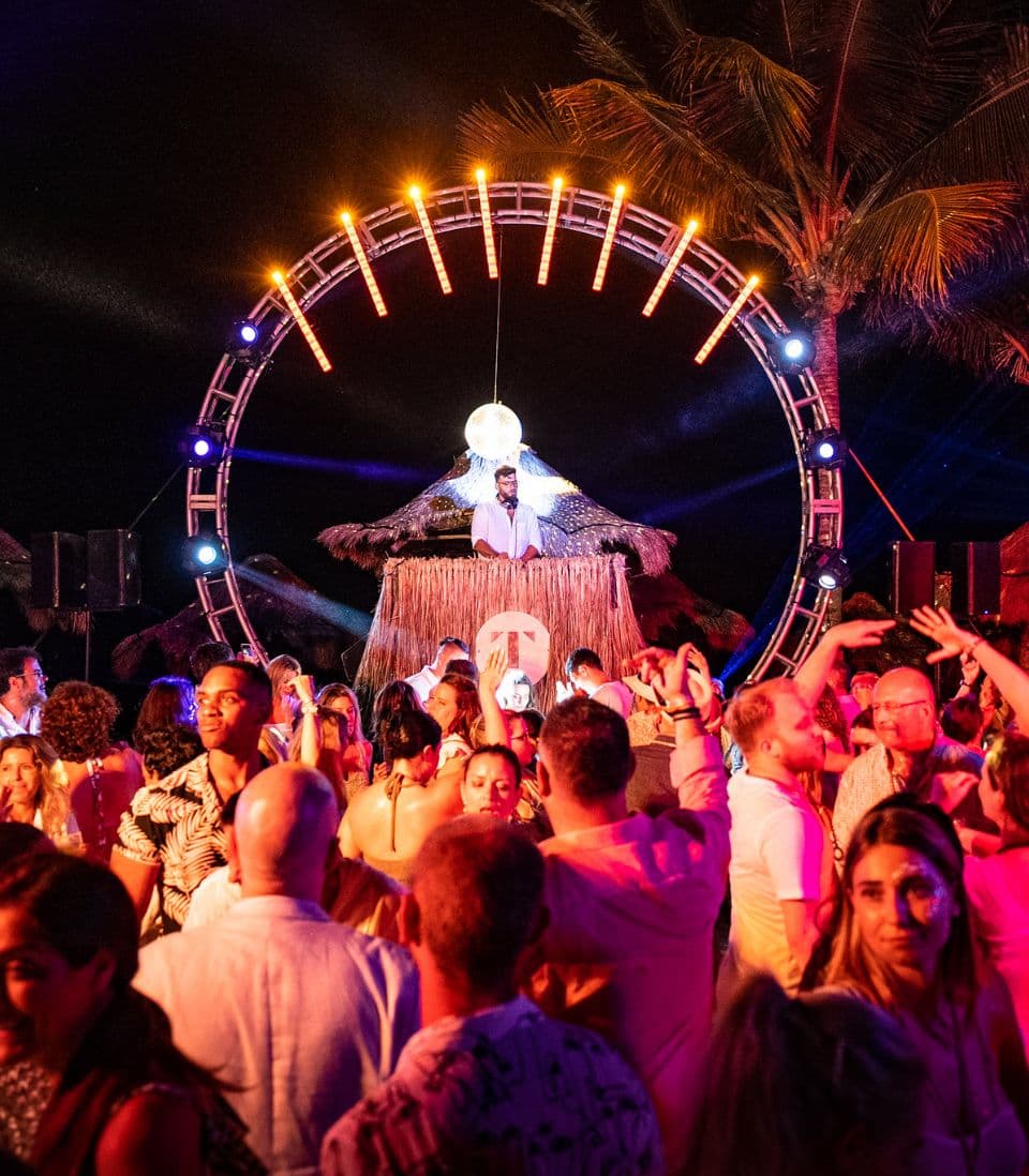 A crowd dancing under a lit ring stage at night